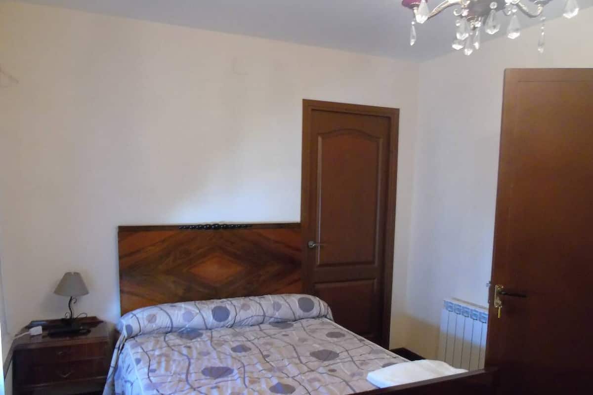 Un dormitorio con cama, mesita de noche, lámpara, puerta de madera y candelabro.