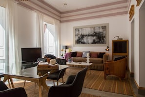 Una sala moderna con una mesa de comedor de vidrio, asientos cómodos, un televisor de pantalla plana y un cuadro abstracto grande en la pared.