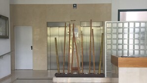 Un ascenseur moderne avec un mur de couleur beige et une enseigne au-dessus. On y trouve un comptoir d’accueil avec un plateau en bois et une cloison en verre.
