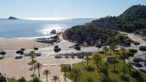 Une vue côtière comprenant une plage, un parking et une zone vallonnée avec des arbres.