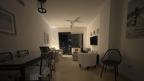 Un salon à l’éclairage tamisé comprenant un coin repas, un ventilateur de plafond et un téléviseur fixé au mur.