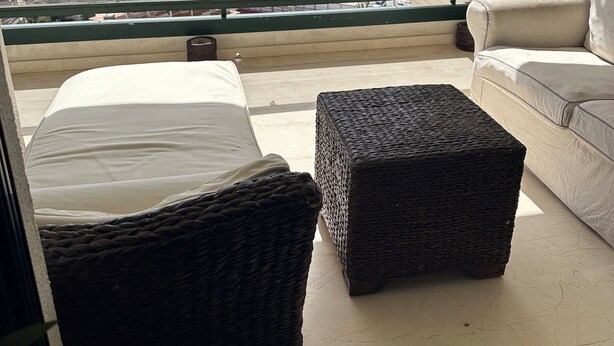 Un balcon aménagé avec un lit, un pouf en osier et un canapé, offrant une vue sur la plage et le paysage urbain.