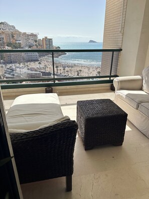 A balcony with a bed, a wicker ottoman, and a sofa, overlooking a beach and cityscape. - Beachfront penthouse with sea views (Villajoyosa)