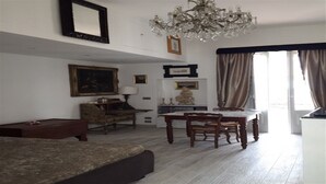 A living room with a sofa, a dining table with chairs, a chandelier, and a large window with curtains. - Detached house in a lovely historic center in Pisticci (Pisticci)