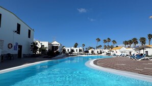 A swimming pool with a curved edge, surrounded by white buildings and palm trees.