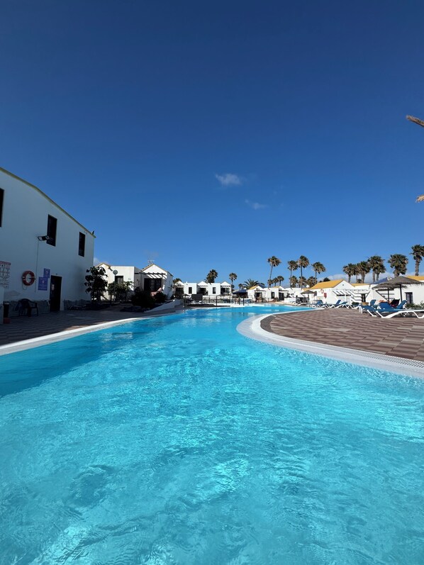 A swimming pool with a curved edge, surrounded by white buildings and palm trees.