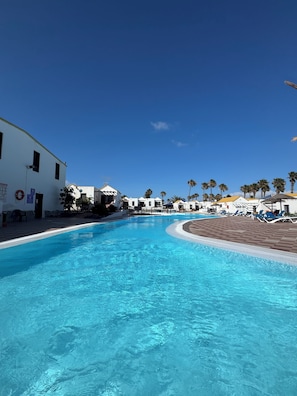 Une piscine à bord incurvé, entourée de bùtiments blancs et de palmiers.