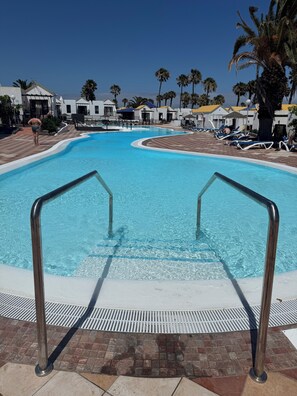 Une piscine entourée de barrières métalliques, de chaises longues et de palmiers.