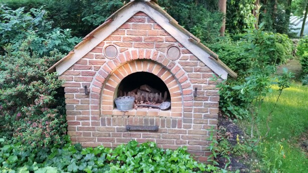 A brick-built outdoor oven with a sloped roof, surrounded by greenery. - Morning sun vacation apartment in a country house with a magnificent garden  (Westerstede)