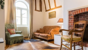 Une pièce chaleureuse avec une cheminée, un fauteuil vert, un canapé à motifs et une chaise en bois.