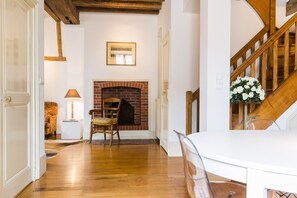 Ein Zimmer mit Kamin, Holzboden, einem Sessel, einem Tisch und einer Treppe.