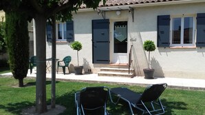 Un bâtiment à l’extérieur blanc, avec une porte d’entrée et deux plantes en pot. On y trouve deux chaises et une table à l’extérieur.