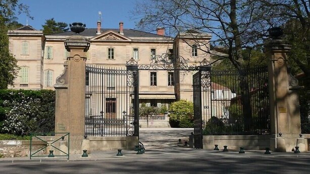 Un grand bâtiment historique doté d’une entrée imposante, avec un portail en fer forgé et une arche centrale.