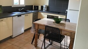 Une cuisine compacte équipée d’un lave-vaisselle, d’un four à micro-ondes, d’une cuisinière et d’un évier. On y trouve une table à manger avec des chaises, et un saladier vert posé dessus.
