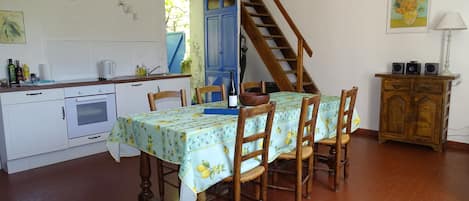 Ein Essbereich mit einem Tisch für vier Personen, Holzstühle, ein Holzschrank, eine Küchenzeile mit Herd und Schränken sowie eine Treppe, die zu einer oberen Ebene führt.