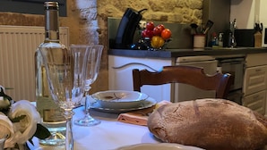 Une table à manger dressée avec des assiettes, une miche de pain, des verres à vin et une bouteille de vin.