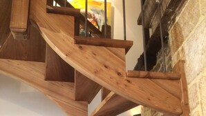 Un escalier en colimaçon en bois, avec un mur de pierres en arrière-plan.