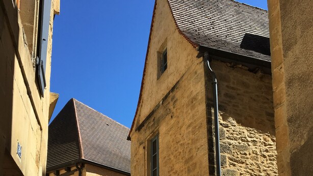 Une ruelle étroite bordée d’immeubles en pierre, avec une porte en métal et un escalier menant à un étage supérieur.