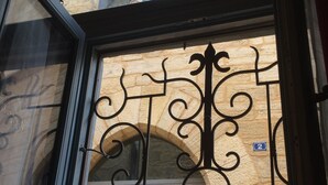 Un portail en fer forgé orné d’un motif de fenêtre gothique, un mur en pierre et une porte en bois portant le numéro « 2 ».