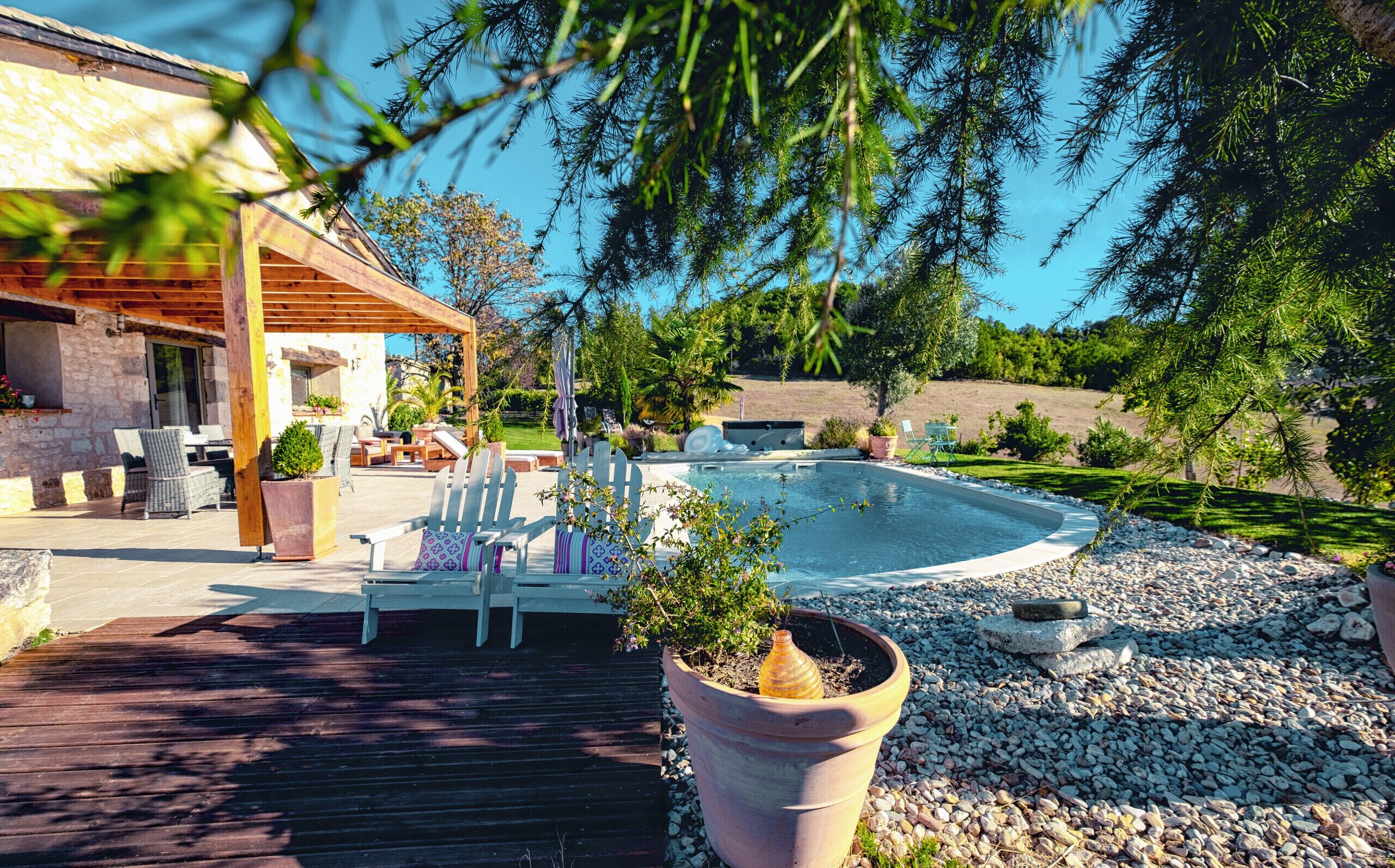 A pool area with lounge chairs, a pergola, and a stone building.