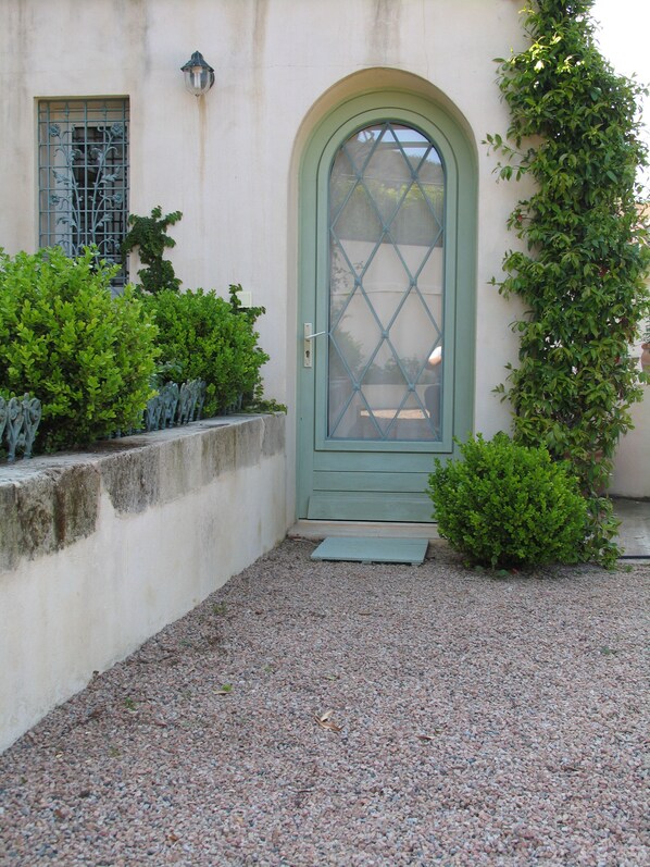 A green door with a diamond-patterned glass panel, a small step leading up to it, and a gravel path.