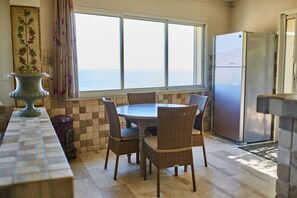 A kitchen with a dining table and chairs, a refrigerator, and a view of the sea.
