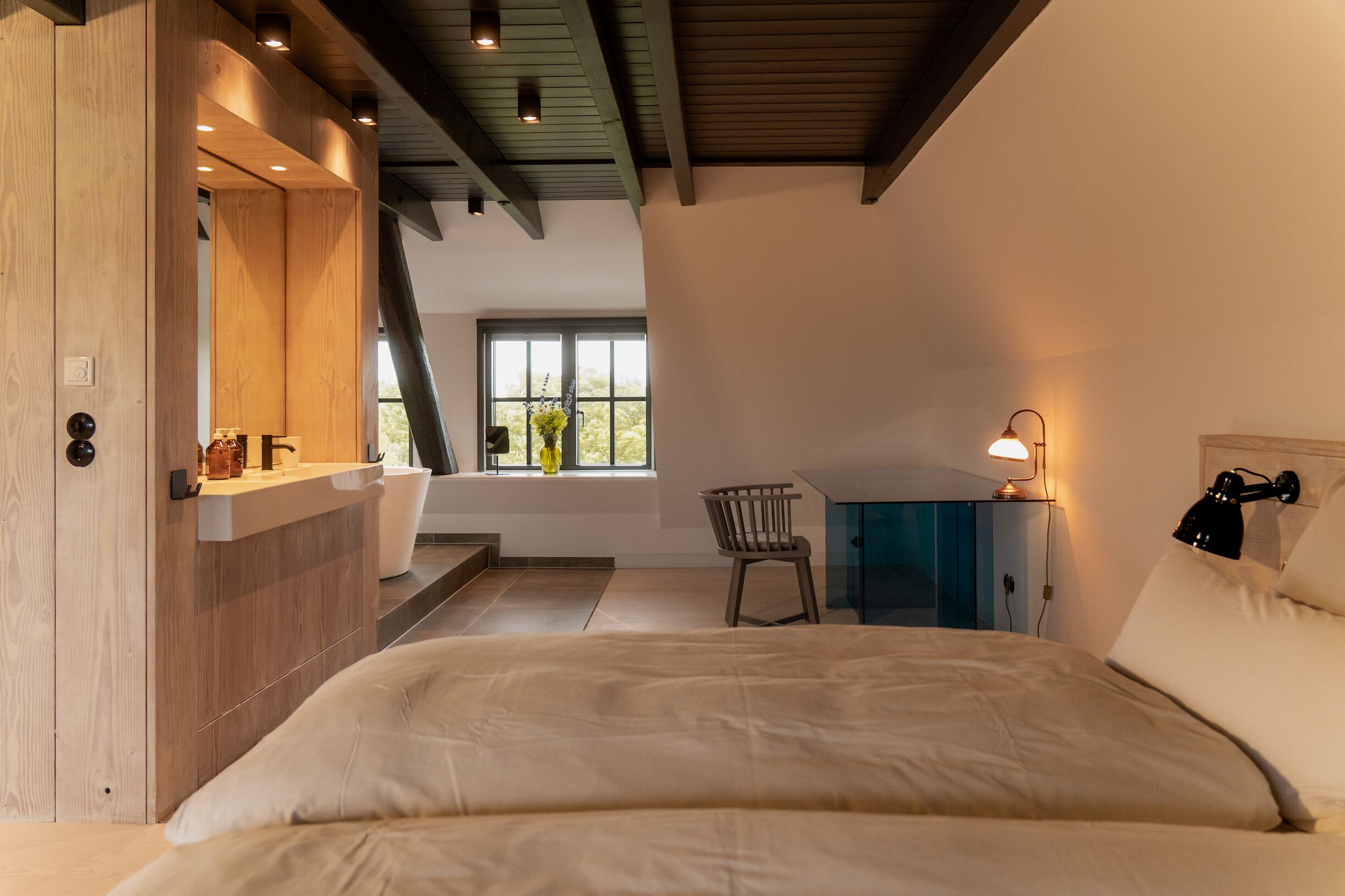 Une chambre à coucher avec un lit, un bureau, une chaise et une fenêtre donnant sur des arbres.