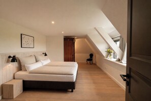 Un dormitorio con cama, lámparas de noche, cabecera de madera, mesita de noche, una silla y una ventana con vistas.