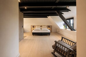 A bedroom with a bed, wooden floor, sloped ceiling, and a window.