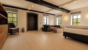 Ein geräumiges Zimmer mit Holzboden, einer dunklen Tür, einem Sofa, einem Sessel und einem Bett.