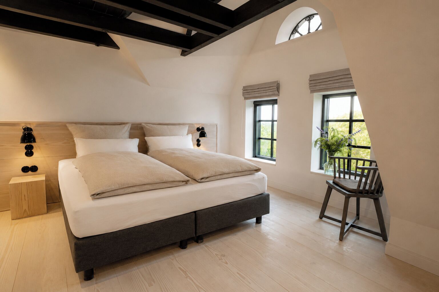 A bedroom with a large bed, a nightstand, a chair, and a window with a view of greenery.