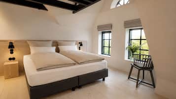 A bedroom with a large bed, a nightstand, a chair, and a window with a view of greenery.