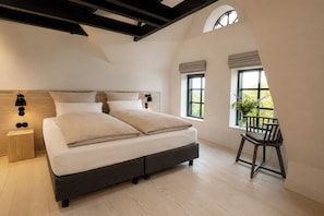 Un dormitorio con una cama grande, una mesita de noche, una silla y una ventana con vista a zonas verdes.