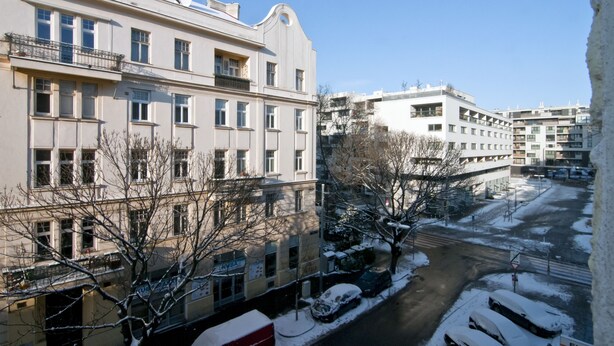 Un edificio de varios pisos con balcones, una calle cubierta de nieve y coches aparcados.