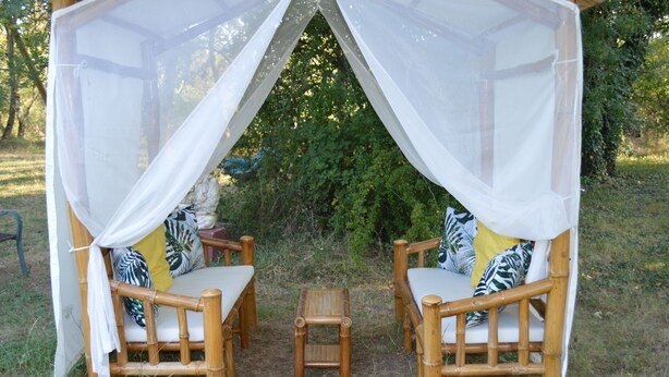 A covered seating area with two chairs and a small table, surrounded by greenery. - Cottage 2 to 5 people (Saint-Clément)