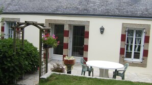 A house with a tiled roof, a wooden pergola with flowers, a white round table with chairs, and a window with curtains. - House in a pastoral setting: 2 or 4 people (Douarnenez)