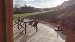 An outdoor patio with a table and chairs, a stone wall, and a view of a hilly landscape. - Cottage Le Meixzoté (Ferdrupt)