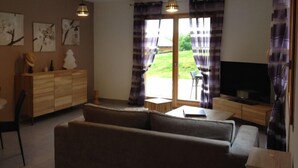 A living room with a sofa, a TV, a wooden cabinet, and a dining area with a table and chairs. - Cottage Le Meixzoté (Ferdrupt)