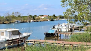 A calm river with boats docked along the shore, surrounded by greenery and a building in the background. - Village apartment  (Agde)