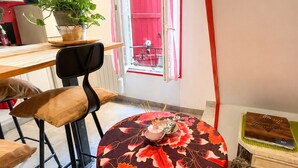 A dining area with a table covered by a floral tablecloth, a chair, and a potted plant. - Village apartment  (Agde)