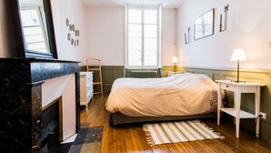 Une chambre à coucher avec un lit, une commode, un miroir, un radiateur et une fenêtre.