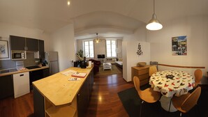 Une cuisine compacte dotée d’un plan de travail en bois, un coin repas avec une table ronde et des chaises, et une vue sur le salon grâce à une porte ouverte.