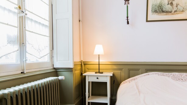 A bedroom with a radiator, a bedside table with a lamp, and a bed. - Le Pasteur, the perfect place in the historical centre of Dijon (up to 4 guests) (Dijon)