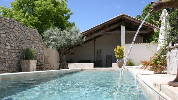 A swimming pool with a stone wall and a wooden pergola.