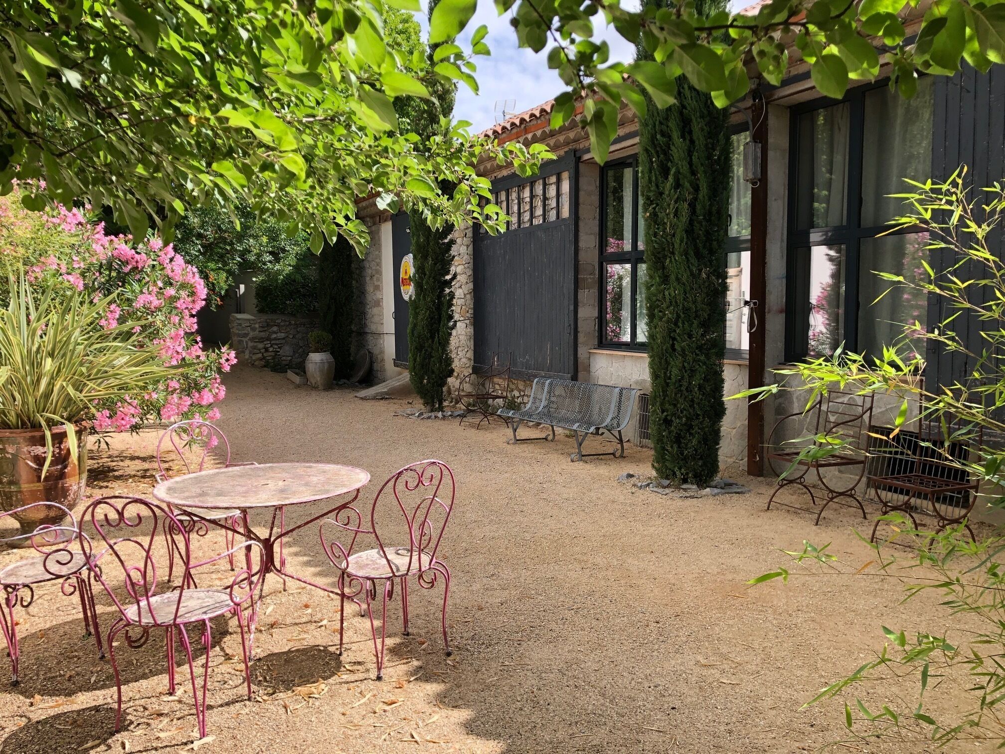 Une cour avec une table ronde et des chaises, entourée de plantes en pot et d’un banc.