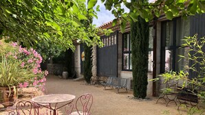 A courtyard with a round table and chairs, surrounded by potted plants and a bench.