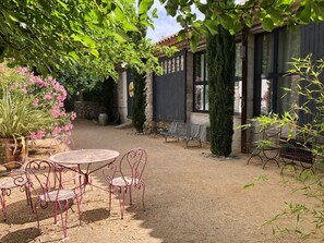 A courtyard with a round table and chairs, surrounded by potted plants and a bench.