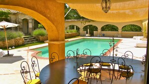 Un espace extérieur avec une piscine, une table ronde et des chaises, le tout entouré de piliers et d’arcs en pierre.