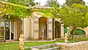 Un bâtiment à la façade en pierre, orné d’une statue à l’entrée, et un jardin agrémenté d’une statue et de quelques marches.