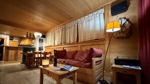 En ombonad träinredning med en soffa, ett bord med en bok, ett ljus och en vinflaska.